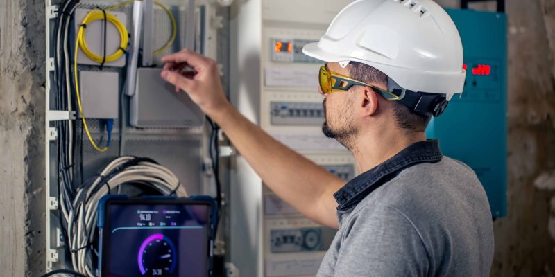 man-electrical-technician-working-switchboard-with-fuses-uses-tablet